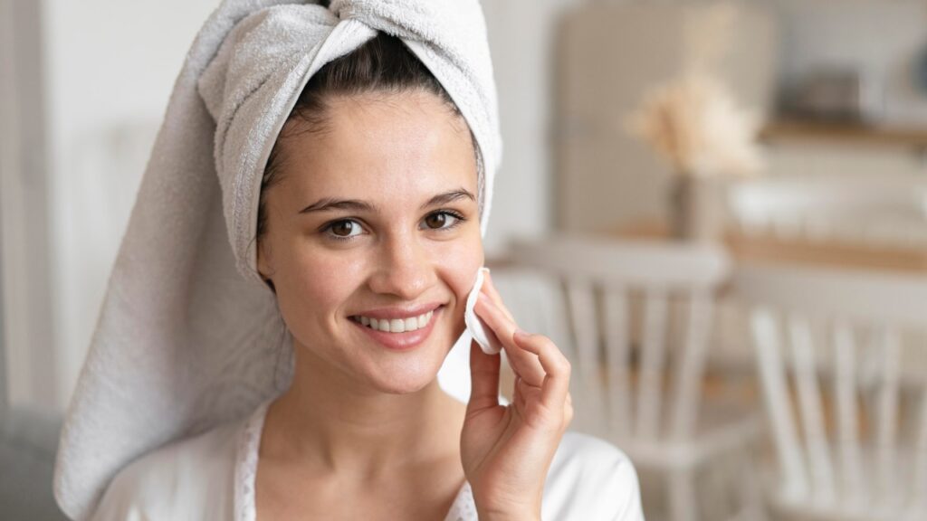 Woman applying rose water skin care toner on her face with cotton pad